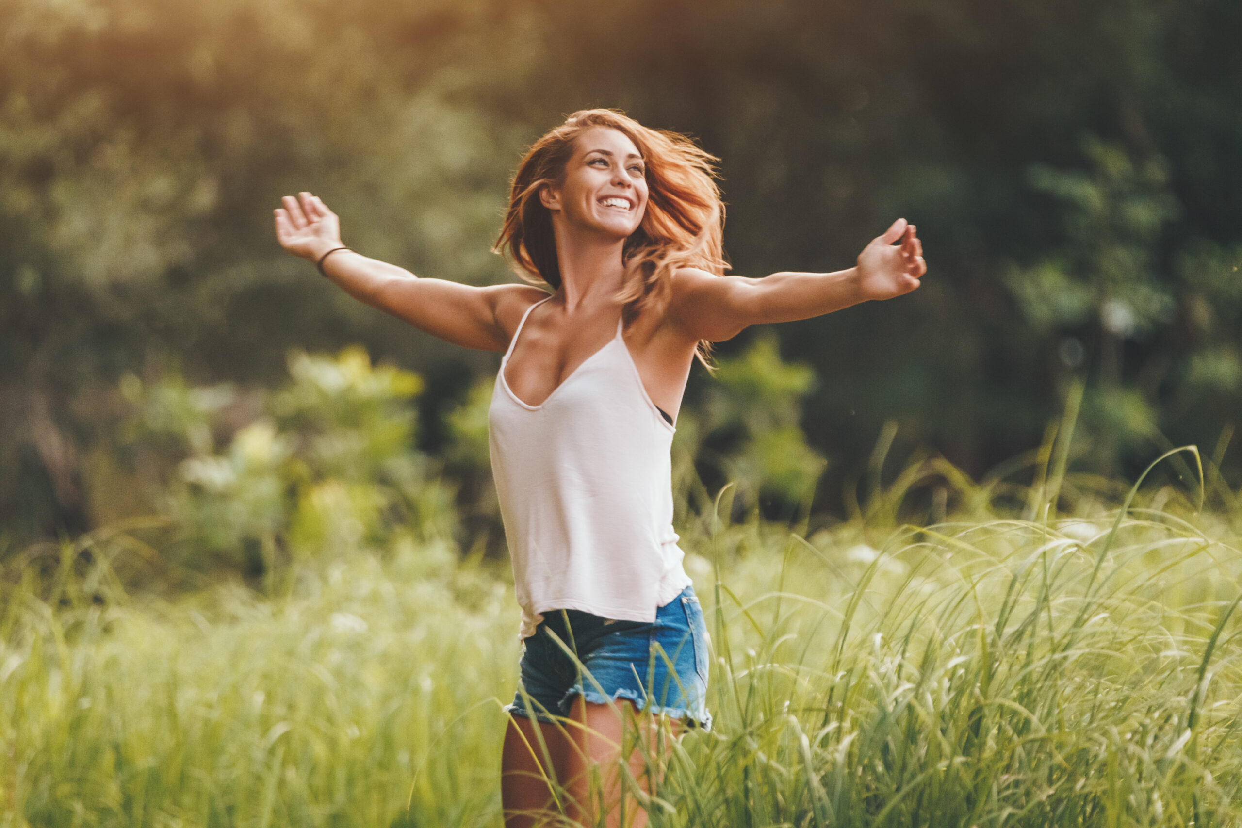 A beautiful young woman is enjoying summer, relaxing and dancing because of happiness in the nature fringed with lush scenery.